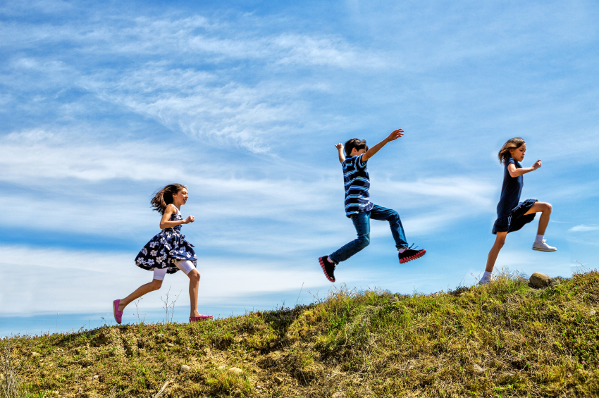 Tre barn som hopper og løper på en gressplen. De er glade.